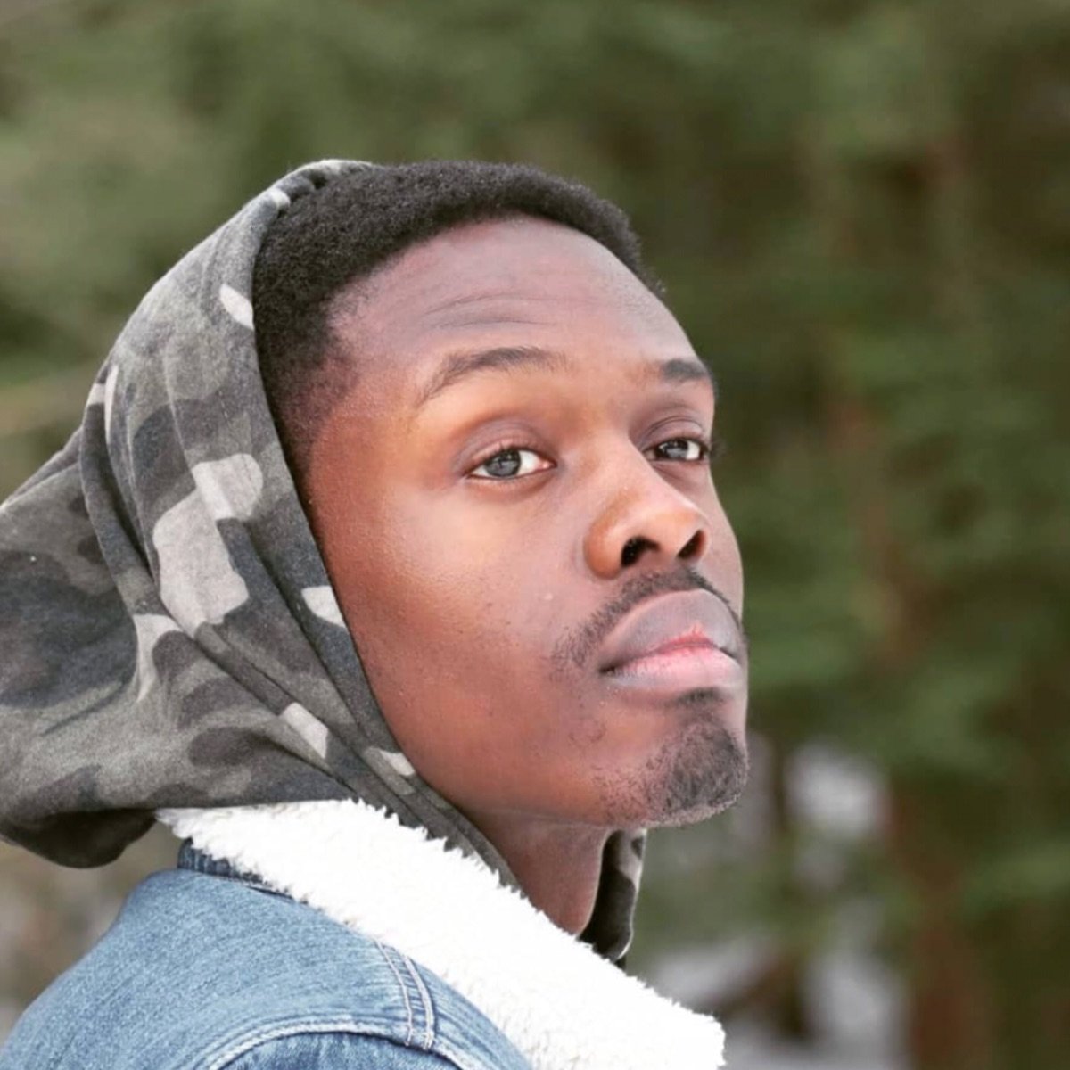 Syness, portrait in a camo hood and denim jacket